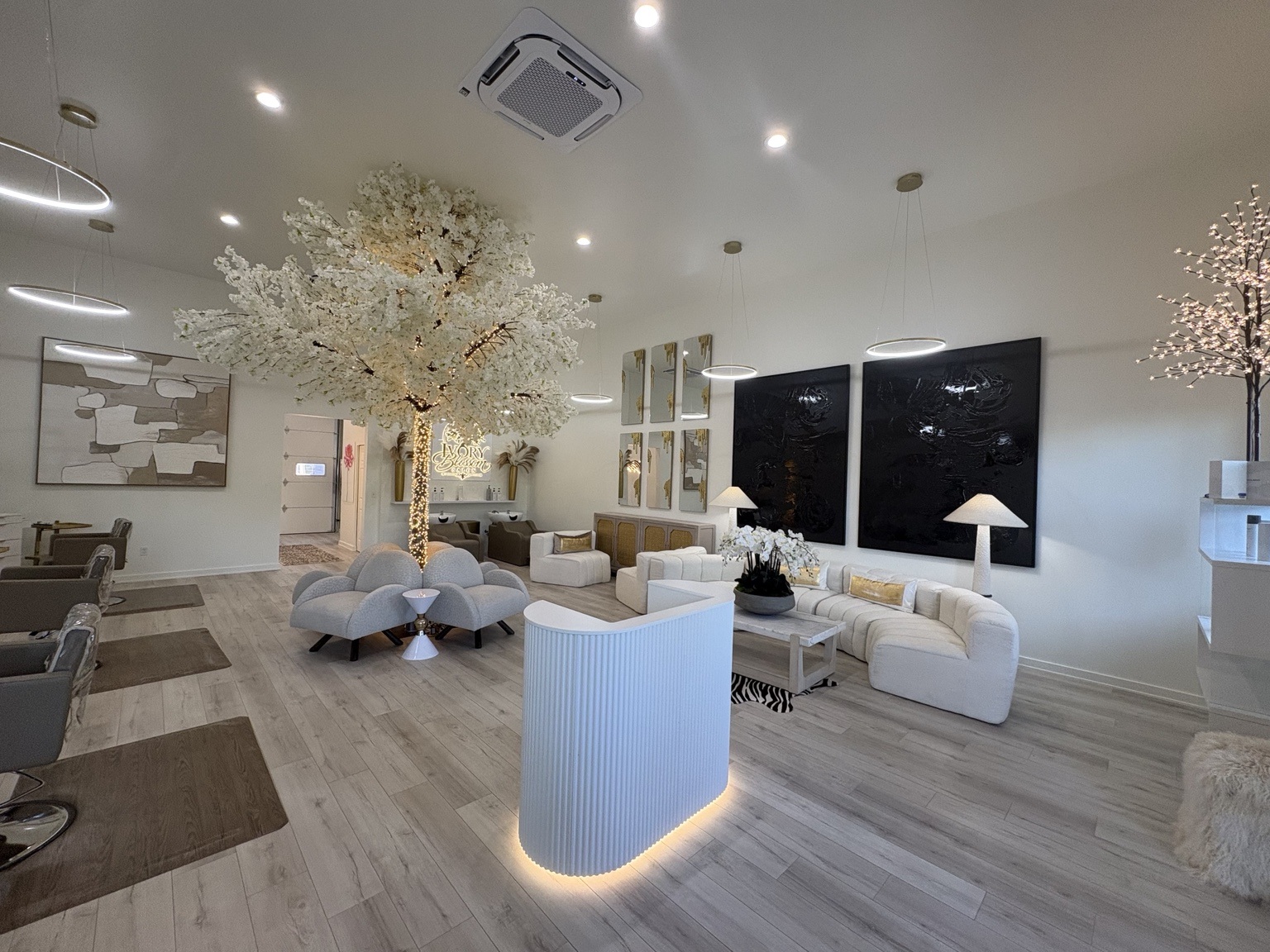 Wide view of Ivory Blossom Salon in Broken Arrow with a glowing reception desk, blossom tree, ivory seating and styling stations